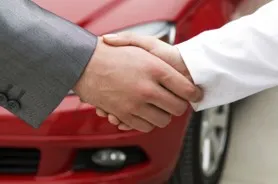 Two people shaking hands over a red car.